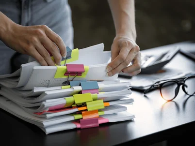 Person am Schreibtisch sucht gezielt in geklemmtem Papierordnern.