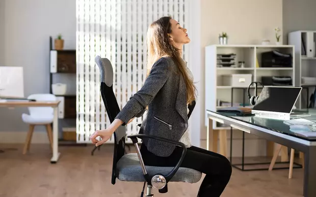 Frau streckt sich vor ihrem Arbeitsplatz im Büro