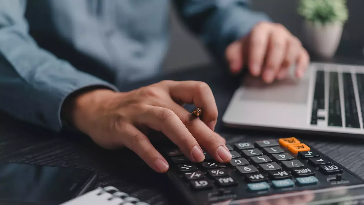 Hände halten einen Stift und benutzen einen Taschenrechner.