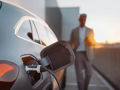 detailbild eines ladenden elektroautos. Im hintergrund unscharf zu sehen ein mann im anzug der auf das auto zugeht